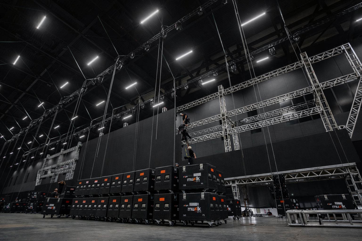 Equipe Muzik Pro em montagem técnica com cases e estruturas de truss em galpão de evento